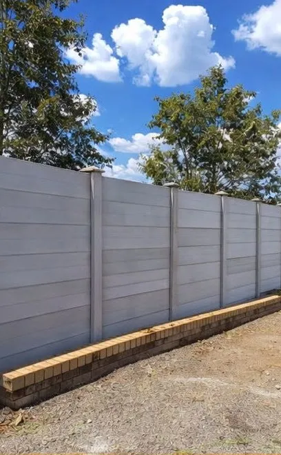 A long, newly installed precast wall on a brick base